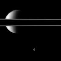 Saturn's rings, made dark in part as the planet casts its shadow across them, cut a striking figure before Saturn's largest moon, Titan. The night side of the planet is to the left, out of the frame of the image. Illuminated Titan can be seen above, below and through gaps in the rings. The moon Mimas (396 km, 246 mi across) is near the bottom of the image. Atlas (30 km, 19 mi across) can barely be detected near the thin F ring just above the center right of the image. (NASA/JPL/SSI)