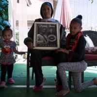 At her home in Las Vegas, Nevada, Trinita Farmer, mother of LVMPD homicide victim, Tashii Brown, poses with portraits of her son and her two granddaughters.  Tashii died after he was tased, punched, and put in an illegal chokehold while having a mental health crisis at The Venetian on Mother's Day, 2017.  March 4, 2018.  Photo by Nissa Tzun, Forced Trajectory Project.  At her home in Las Vegas, Nevada, Trinita Farmer, mother of LVMPD homicide victim, Tashii Brown, poses with portraits of her son and her two granddaughters.  Tashii died after he was tased, punched, and put in an illegal chokehold while having a mental health crisis at The Venetian on Mother's Day, 2017.  March 4, 2018.  Photo by Nissa Tzun, Forced Trajectory Project.