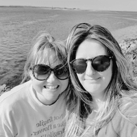 Photo shows two women, Ceryn Rowntree (left) and Charlie Edwards (right) both outdoors and smiling at the camera. Both women are in their 40s with long dark hair and large sunglasses.