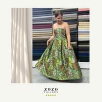 Young woman swirls the silk brocade skirt of her bespoke tailored ball gown in the An Bang studio of her Hoi An tailor.