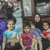 "We moved from Miasar, eastern from Aleppo, the city has been taken by Al Nosra. We've left two and a half year ago now, we were the last ones to leave the block. It was our house, we had just finished paying it. Little by little, the city was emptied and the bombs were falling, we were too scared. A three-bedroom house with a living room, the kids liked to play on the balcony, and we've abandonned it.   I know everything that was inside has been stolen shortly after we left, and now it's probably been destroyed. We've left with two blankets and the clothes we had on us, that's all. We were moved to that room. When the first mortar fell here a couple of years ago, my son got injured. Mortars always come in groupe, always two or three, but he ran to see what happened. That little demon told his teacher I sent him on the street to buy some groceries, luckily h's still alive.  We live in 14 square meters since those last few years. We're eight – six of us are children. We suffocate but we thank god for being still alive. I was offered to go live in some place bigger, but it's the shell of a building, they are no walls, no toilets, no water, we can't.   My husband can't work, he's almost blind, so to make a living I gather some clothes a merchant gives me for free, I sell what I can and I get a small percentage of the sales. I've told all the neighbors I had some clothes, and those who want to help us sometimes buy some. I don't do some bookkeeping, everything I own I spend, but I make a bit less than 5000 pounds a month (10€), every two weeks I try to buy a bit of chicken.   We didn't have this life before, we worked all of our lives to build what we've lost, but we stay positive, the war will stop and we'll be stronger, we'll build it again. We'll get through this."
