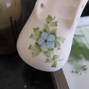A close up of an in progress hand painted blue forget-me-not and foliage on the toe of a porcelain baby shoe.