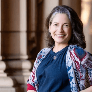PIcture of Dr. Ferguson wearing blue shirt and red and blue flowered shawl, standing in front of columns in Balboa Park, San Diego. Photo Credit: Xavier Bailey Photography PIcture of Dr. Ferguson wearing blue shirt and red and blue flowered shawl, standing in front of columns in Balboa Park, San Diego. Photo Credit: Xavier Bailey Photography