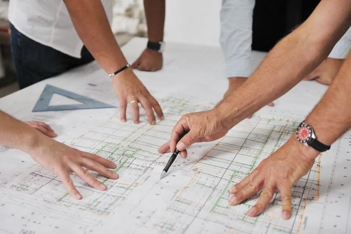 a project team are marking up a set of building plans on a large desk a project team are marking up a set of building plans on a large desk