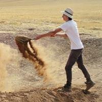 A man standing on a mountain of dirt empting a shovel of dirt A man standing on a mountain of dirt empting a shovel of dirt