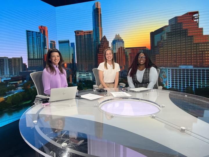 Stephanie and Ki'ana sitting at a news desk with Katie Jackson, in front of a screen showing the Austin skyline. Stephanie and Ki'ana sitting at a news desk with Katie Jackson, in front of a screen showing the Austin skyline.