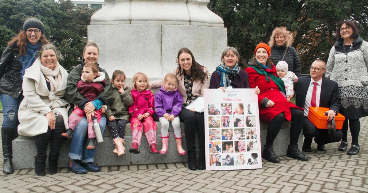 A group of women and children ae sitting on a monument outside parliament. One is holding a poster. In the centre is former Prime Minister Jacinda Ardern next to one of the young girls. A group of women and children ae sitting on a monument outside parliament. One is holding a poster. In the centre is former Prime Minister Jacinda Ardern next to one of the young girls.