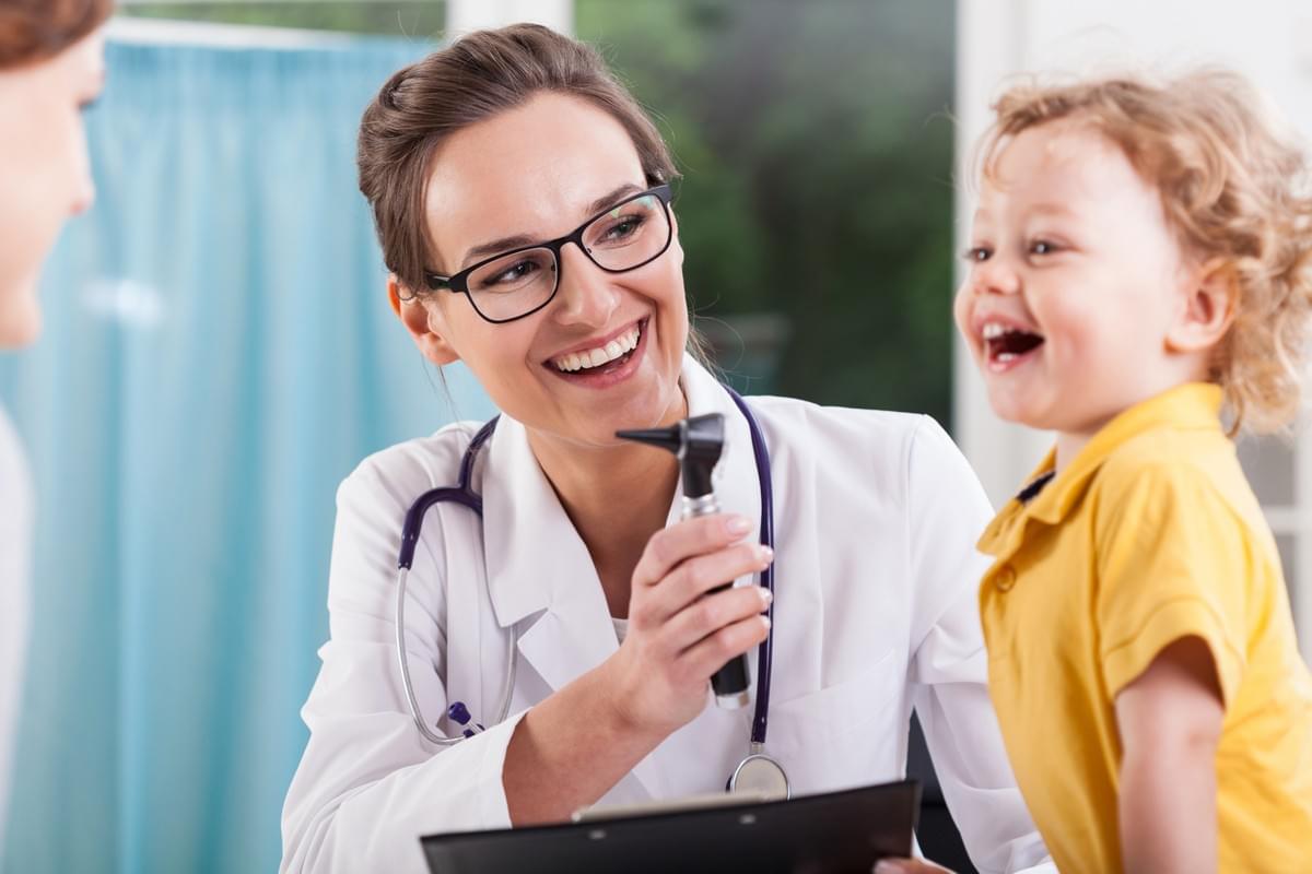 Woman Doctor Examining a Small Boy in a Yellow Shirt Talking to Mom about Compounded Medication Woman Doctor Examining a Small Boy in a Yellow Shirt Talking to Mom about Compounded Medication