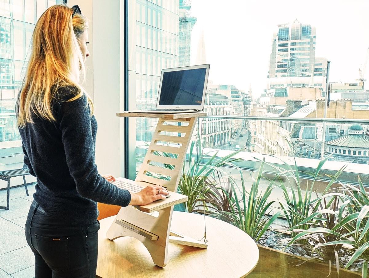 Woman standing at desk, using raised computer stand overlooking a city view Woman standing at desk, using raised computer stand overlooking a city view
