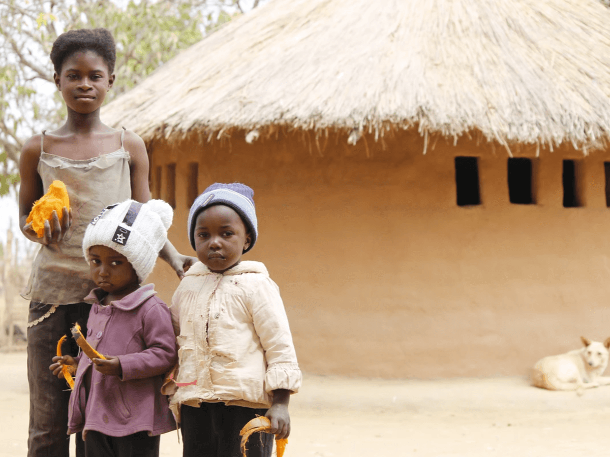 three african children standing in front of a mud hut three african children standing in front of a mud hut