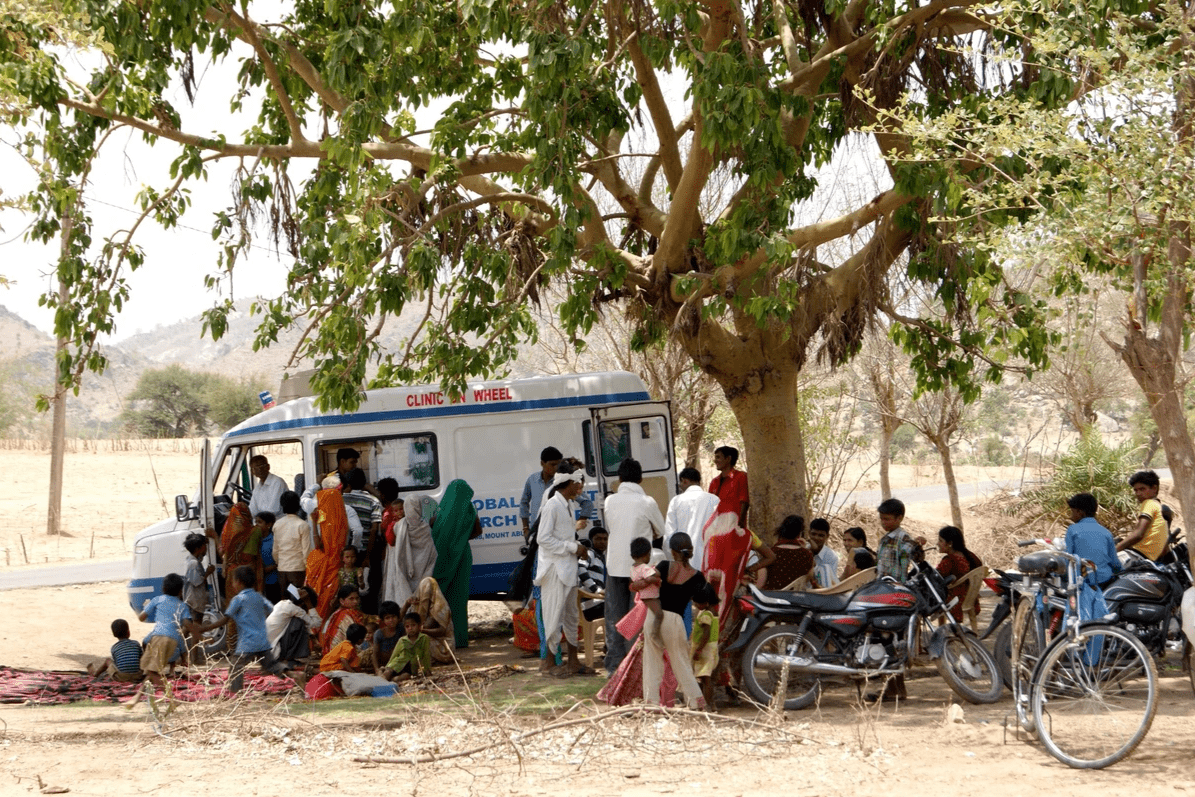 A crowd of people sitting under a tree waiting to be seen by the mobile clinic. A crowd of people sitting under a tree waiting to be seen by the mobile clinic.