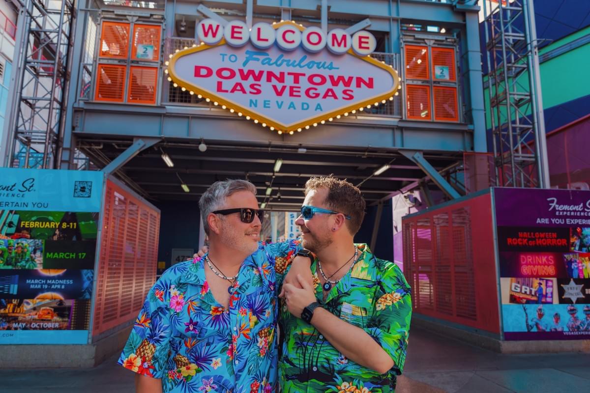 Couple smiling and holding hands in front of the Fremont Street welcome sign in downtown Las Vegas, surrounded by neon lights and vintage charm. Couple smiling and holding hands in front of the Fremont Street welcome sign in downtown Las Vegas, surrounded by neon lights and vintage charm.