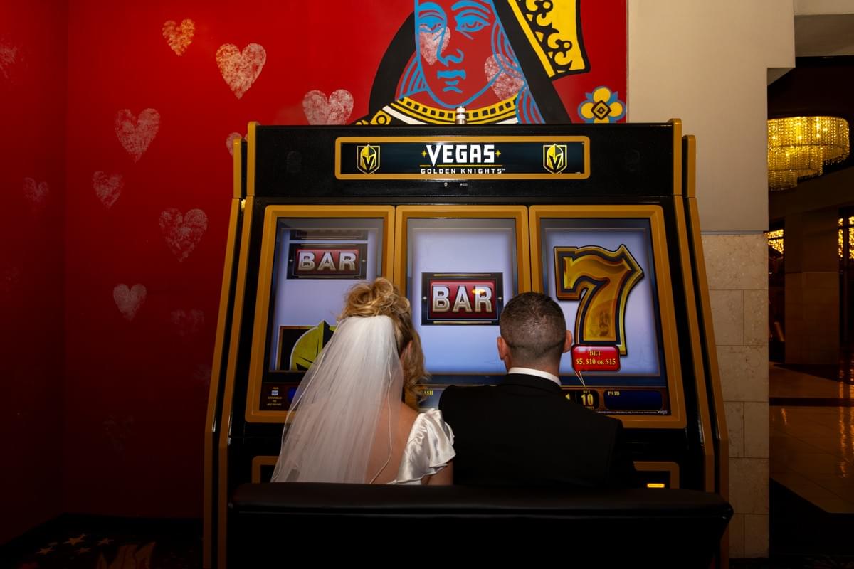 Newlywed couple posing in front of a giant Vegas-themed casino slot machine after their same-day wedding. Newlywed couple posing in front of a giant Vegas-themed casino slot machine after their same-day wedding.