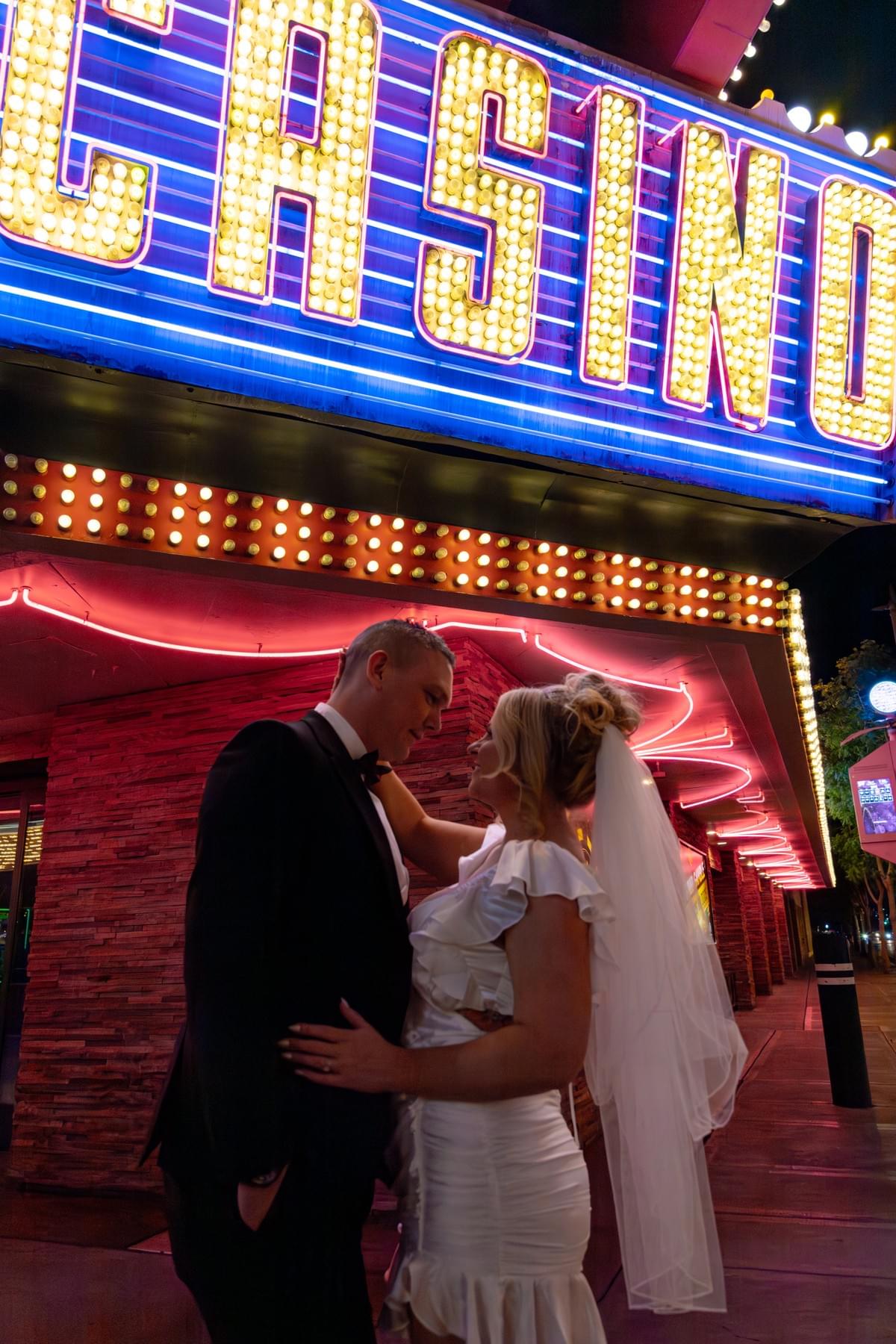 Couple in wedding attire standing under neon lights that say 'Casino' in Las Vegas, captured during their elopement. Couple in wedding attire standing under neon lights that say 'Casino' in Las Vegas, captured during their elopement.