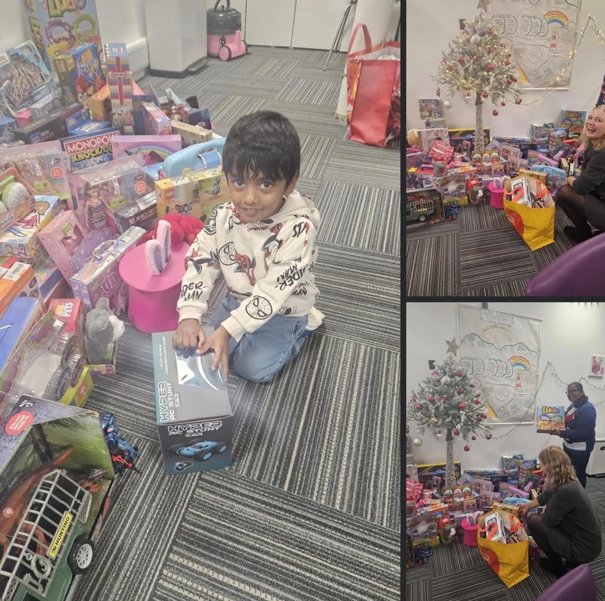 A child sits on the floor smiling and holding a toy box, surrounded by donated toys near a decorated Christmas tree . A child sits on the floor smiling and holding a toy box, surrounded by donated toys near a decorated Christmas tree .