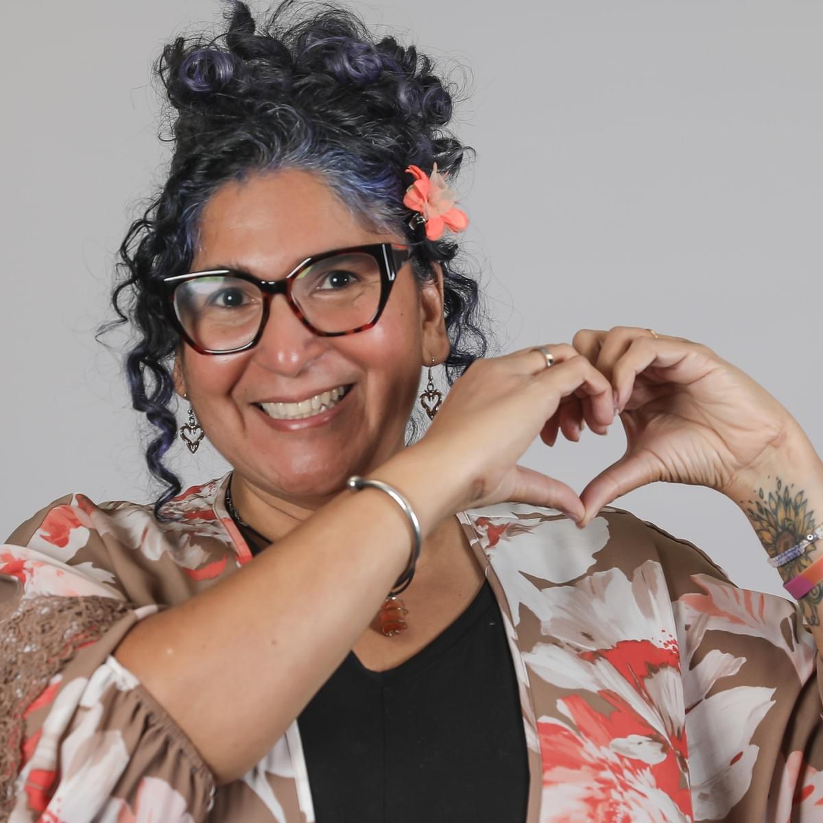 a smiling bespectacled woman wearing an orange and beige floral top a smiling bespectacled woman wearing an orange and beige floral top