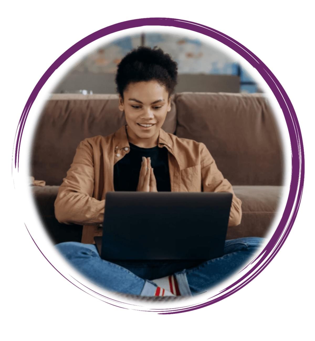 A person sits cross-legged on a round cushion indoors, with a laptop resting on their lap. Their hands are pressed together in front of their chest in a gesture that could signify greeting, gratitude, or mindfulness—suggesting they are engaged in a virtual interaction such as a video call, online class, or meditation session. Behind them is a cozy brown sofa adorned with a green pillow and a textured brown knitted blanket draped over the armrest. A modern floor lamp with a white shade stands nearby, and a piece of abstract wall art in cool blue tones hangs above the sofa. The setting is warm and inviting, blending digital engagement with personal comfort. The composition reflects contemporary lifestyles that integrate technology, emotional presence, and home-based connection A person sits cross-legged on a round cushion indoors, with a laptop resting on their lap. Their hands are pressed together in front of their chest in a gesture that could signify greeting, gratitude, or mindfulness—suggesting they are engaged in a virtual interaction such as a video call, online class, or meditation session. Behind them is a cozy brown sofa adorned with a green pillow and a textured brown knitted blanket draped over the armrest. A modern floor lamp with a white shade stands nearby, and a piece of abstract wall art in cool blue tones hangs above the sofa. The setting is warm and inviting, blending digital engagement with personal comfort. The composition reflects contemporary lifestyles that integrate technology, emotional presence, and home-based connection
