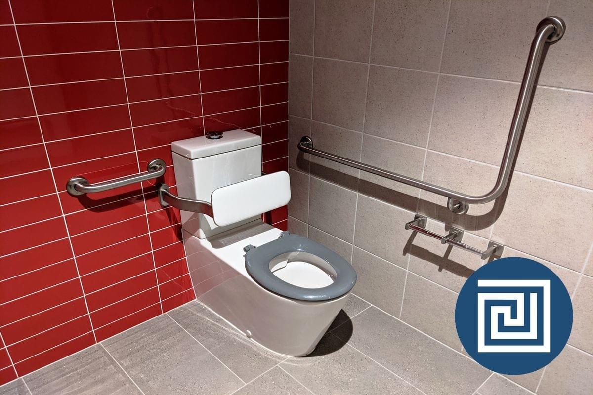 An accessible toilet in a corner of a room with a grey seat and grabrails An accessible toilet in a corner of a room with a grey seat and grabrails