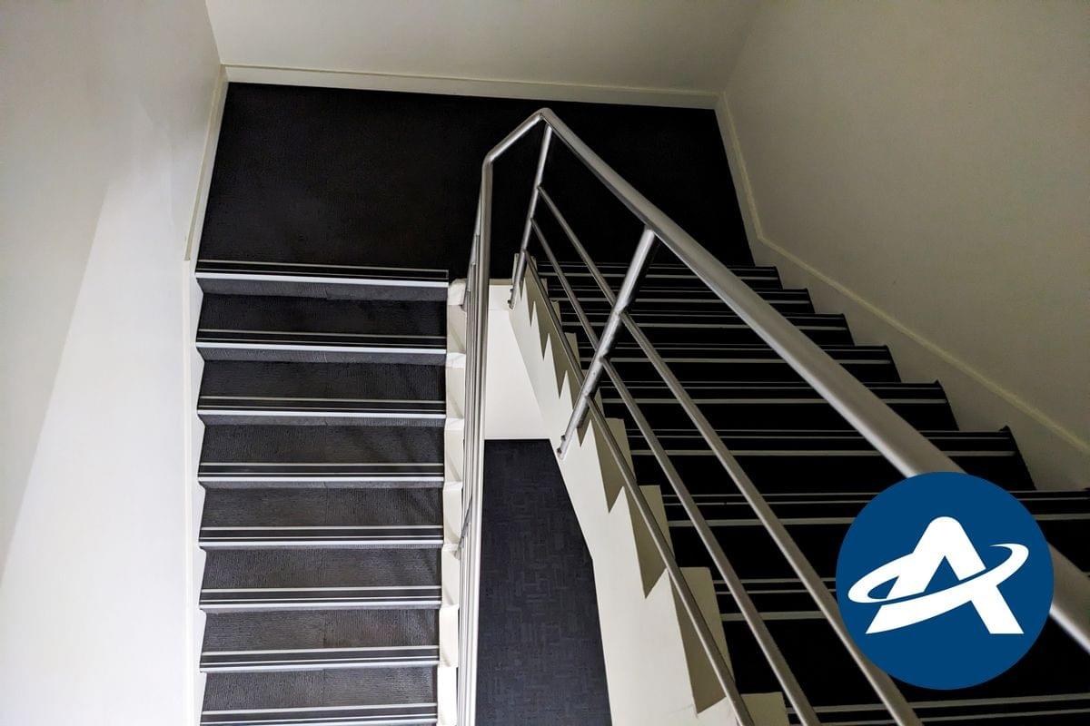 A view looking down a modern stairway with a single stainless steel handrail and non-compliant tread nosing strips (2) A view looking down a modern stairway with a single stainless steel handrail and non-compliant tread nosing strips (2)