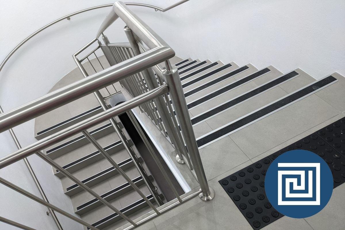 A view looking down a modern stairway with stainless steel handrails, black tread nosing strips and black tactile indicators A view looking down a modern stairway with stainless steel handrails, black tread nosing strips and black tactile indicators