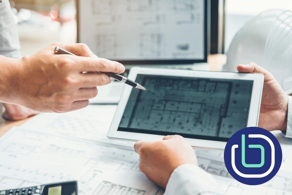 Two architects are seated at a desk, one is holding a tablet PC, while the other is pointing towards the architectural drawing on the screen Two architects are seated at a desk, one is holding a tablet PC, while the other is pointing towards the architectural drawing on the screen