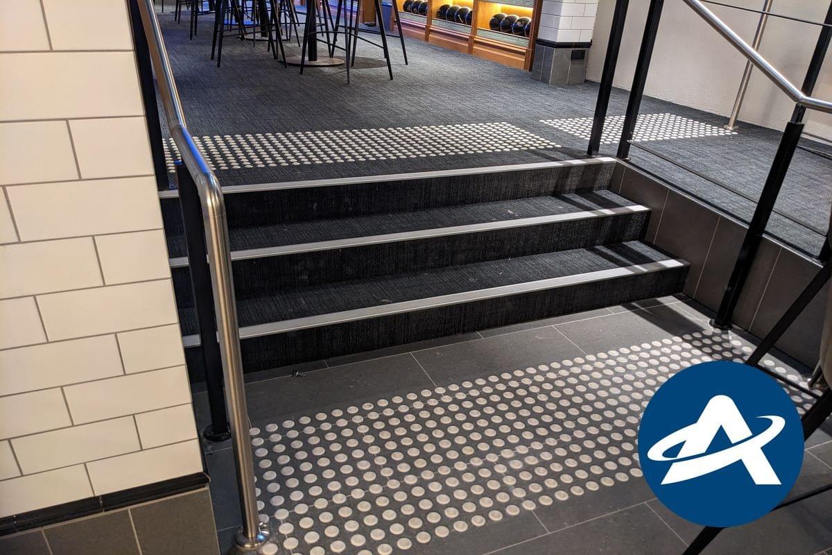 A small three step internal stairway, with black carpet, stainless steel handrails, tactile indicators, and silver coloured tread nosing strips (2) A small three step internal stairway, with black carpet, stainless steel handrails, tactile indicators, and silver coloured tread nosing strips (2)