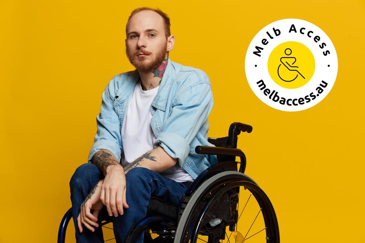 A man in a wheelchair looks at the camera, with tattoos on his arms sits on a yellow studio background with logo A man in a wheelchair looks at the camera, with tattoos on his arms sits on a yellow studio background with logo
