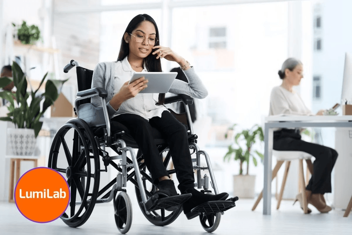 A woman in a wheelchair uses a tablet in an office, with another person working at a desk in the background. A woman in a wheelchair uses a tablet in an office, with another person working at a desk in the background.
