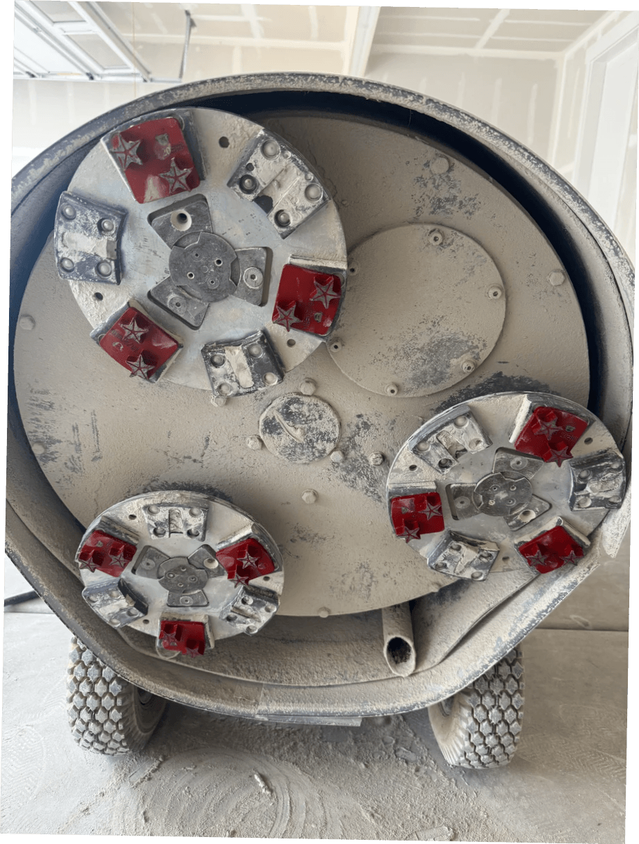 Underside of a planetary floor grinder fitted with red Husqvarna Redi-Lock style 16/20 hard bond cap cutters and metal grinding tools during a concrete surface preparation test for penetrating sealer absorption. Underside of a planetary floor grinder fitted with red Husqvarna Redi-Lock style 16/20 hard bond cap cutters and metal grinding tools during a concrete surface preparation test for penetrating sealer absorption.