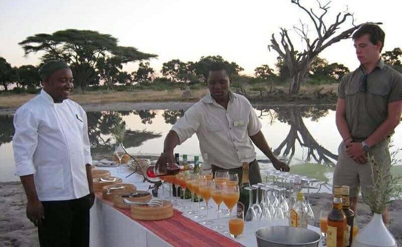 Host preparing sundowners outdoors, setting up drinks and snacks in a scenic bush setting at sunset. Host preparing sundowners outdoors, setting up drinks and snacks in a scenic bush setting at sunset.