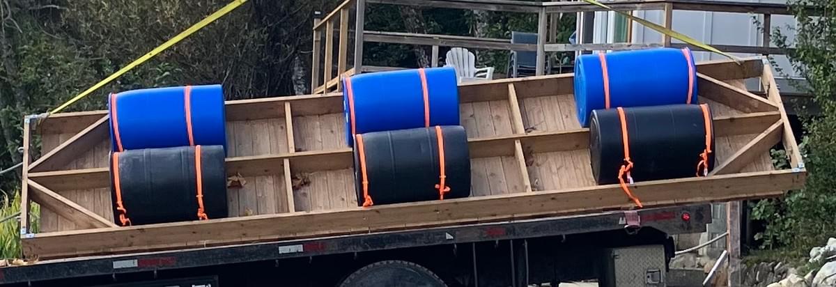 one blue one black 55 gallon plastic barrells are fastened to the underside of a dock using orange gear straps. one blue one black 55 gallon plastic barrells are fastened to the underside of a dock using orange gear straps.