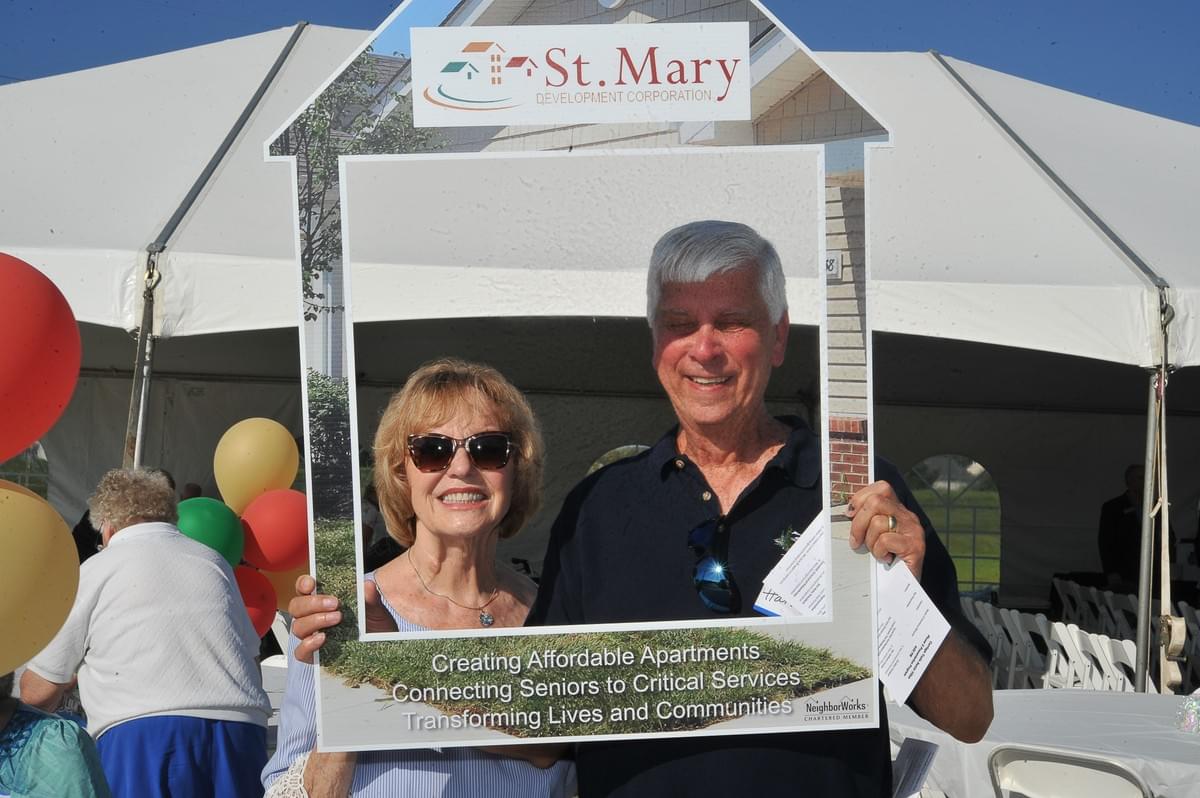 Two people outside a St. Mary event holding a house sign Two people outside a St. Mary event holding a house sign