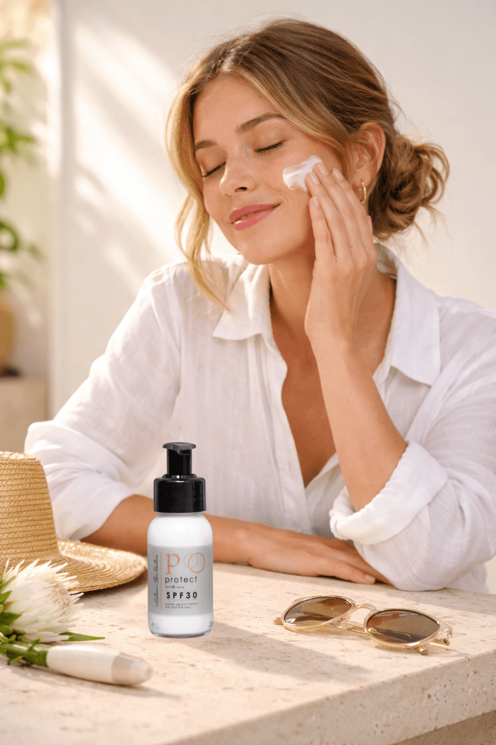 ve white woman in her mid-twenties with fair freckled skin, soft honey-blonde hair loosely tied in a low bun with face-framing wisps, natural minimal makeup with a fresh sun-kissed complexion — wearing a white linen button-down shirt with the sleeves casually rolled to the elbows, suggesting a bright South African morning outdoor lifestyle. She sits at a smooth warm white travertine stone outdoor-style studio countertop inside a professional photography studio. The inBetween Skin Routine Protect SPF30 50ml compact clear glass bottle with its white SPF cream content, ve white woman in her mid-twenties with fair freckled skin, soft honey-blonde hair loosely tied in a low bun with face-framing wisps, natural minimal makeup with a fresh sun-kissed complexion — wearing a white linen button-down shirt with the sleeves casually rolled to the elbows, suggesting a bright South African morning outdoor lifestyle. She sits at a smooth warm white travertine stone outdoor-style studio countertop inside a professional photography studio. The inBetween Skin Routine Protect SPF30 50ml compact clear glass bottle with its white SPF cream content,