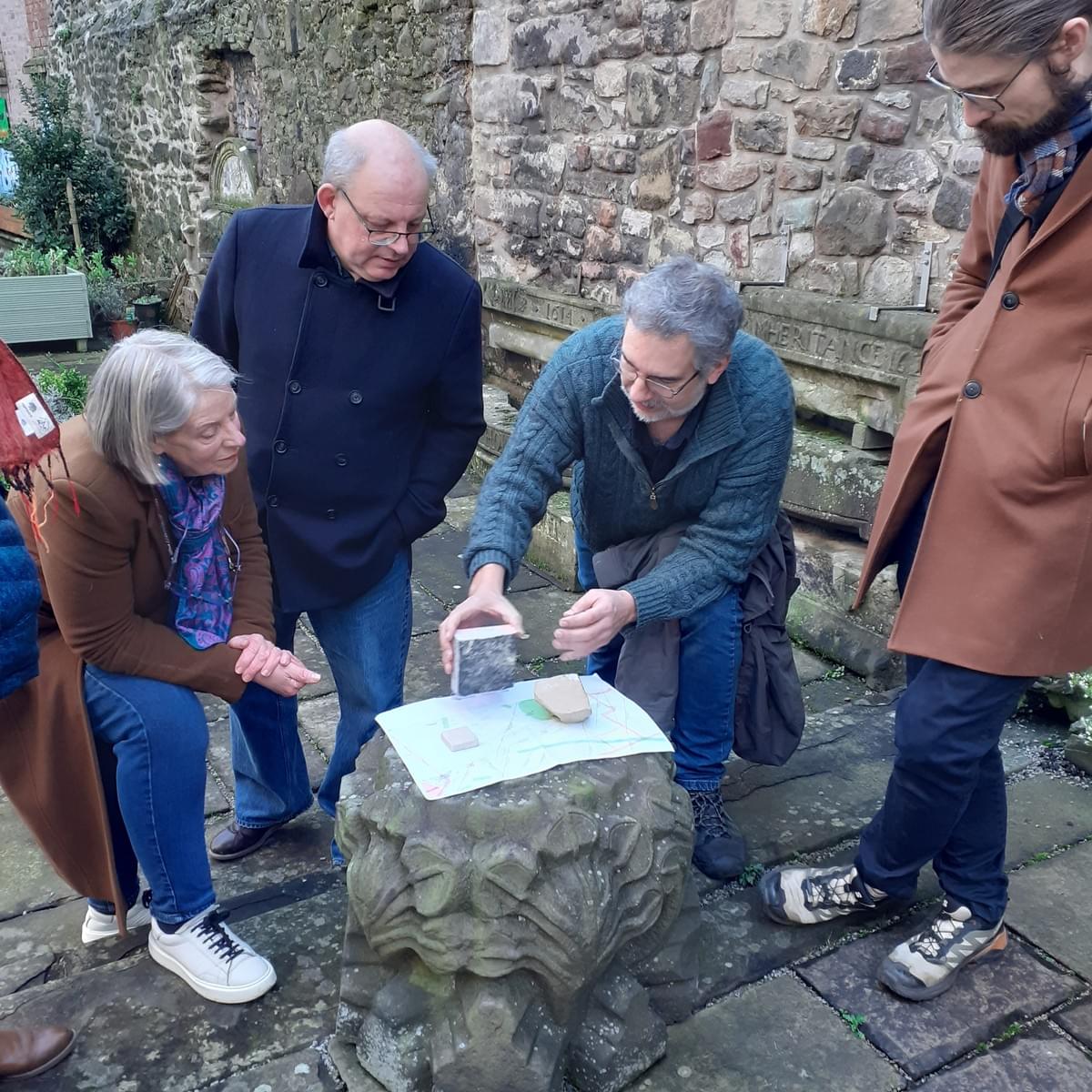 A group of four people look at some small stone samples resting on an elaborately carved medieval stone boss in the Museum of Edinburgh courtyard. A group of four people look at some small stone samples resting on an elaborately carved medieval stone boss in the Museum of Edinburgh courtyard.
