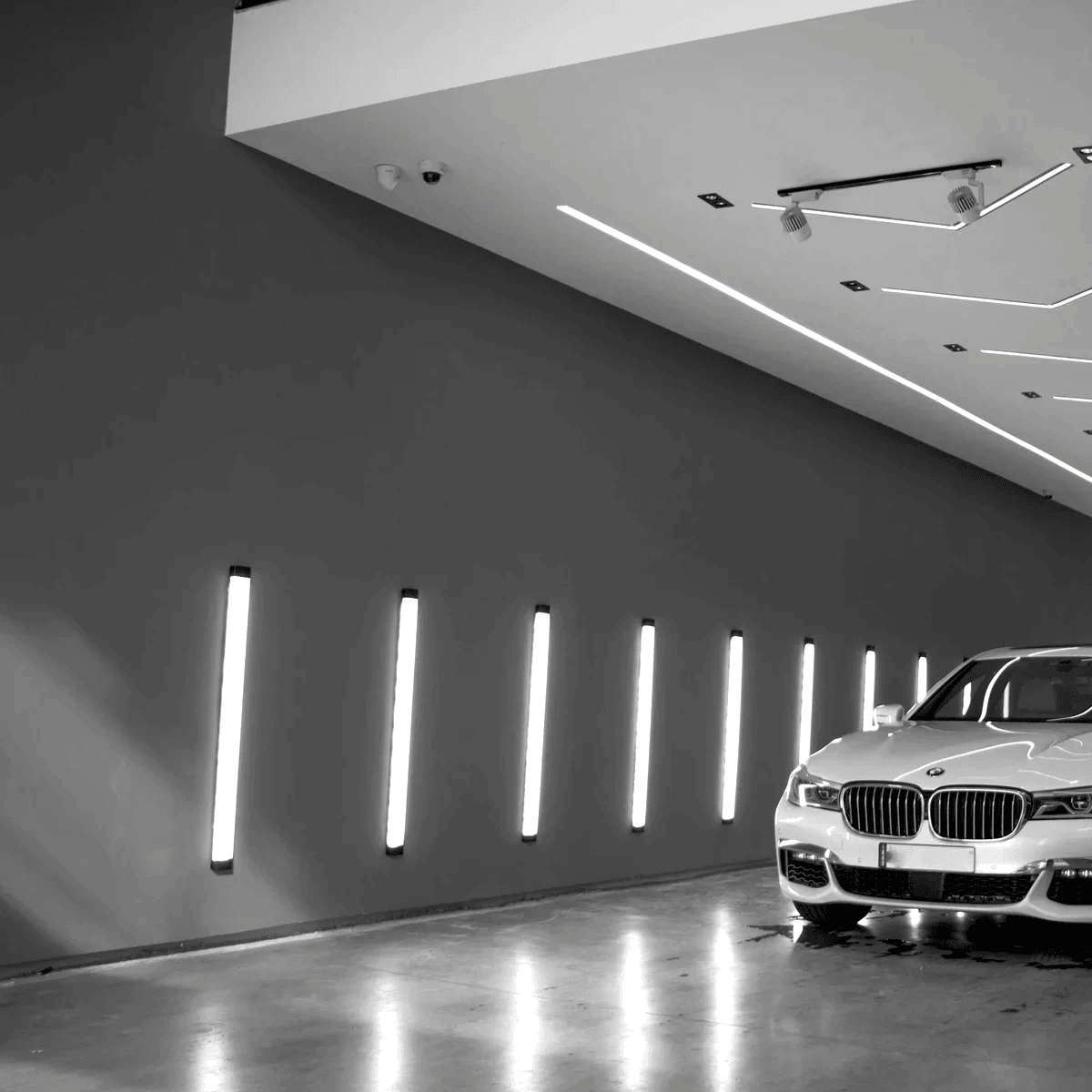 A black and white garage displaying LED lights on the walls and a BMW white car being parked A black and white garage displaying LED lights on the walls and a BMW white car being parked