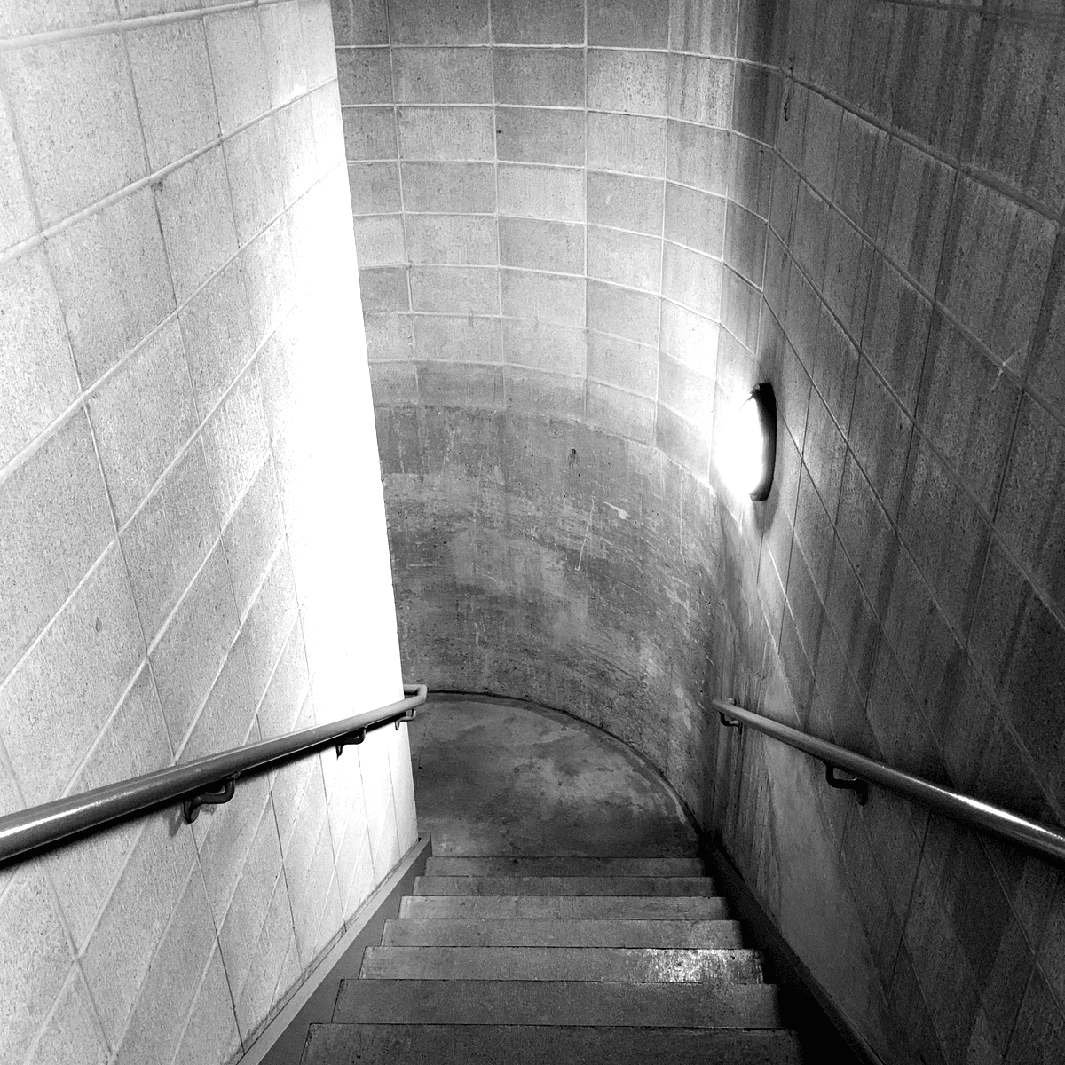 A black and white staircase leading to an underground basement with metal railings and a wall light A black and white staircase leading to an underground basement with metal railings and a wall light
