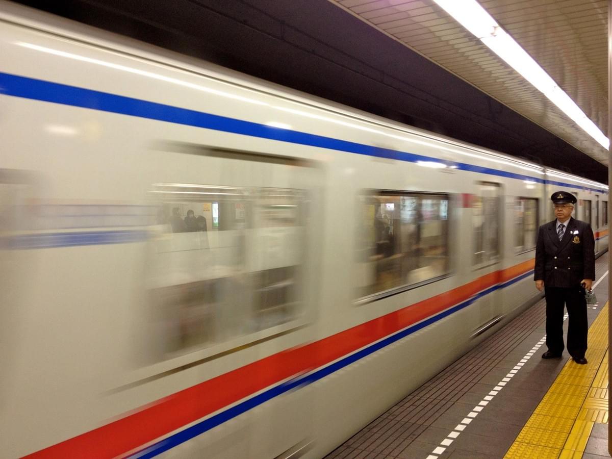 Train in motion at a Japanese station with a station staff member standing on the platform Train in motion at a Japanese station with a station staff member standing on the platform