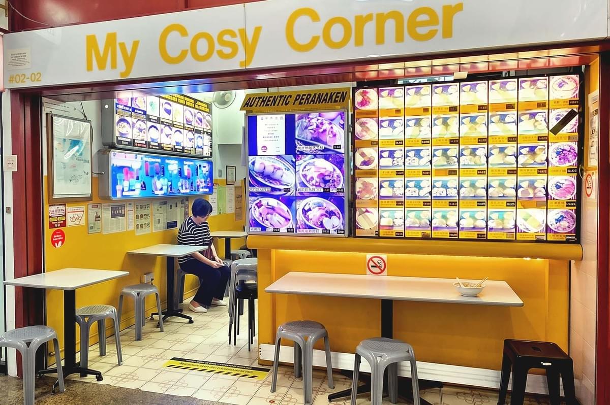 My Cosy Corner storefront with visible display of available dishes and a lady waiting inside My Cosy Corner storefront with visible display of available dishes and a lady waiting inside