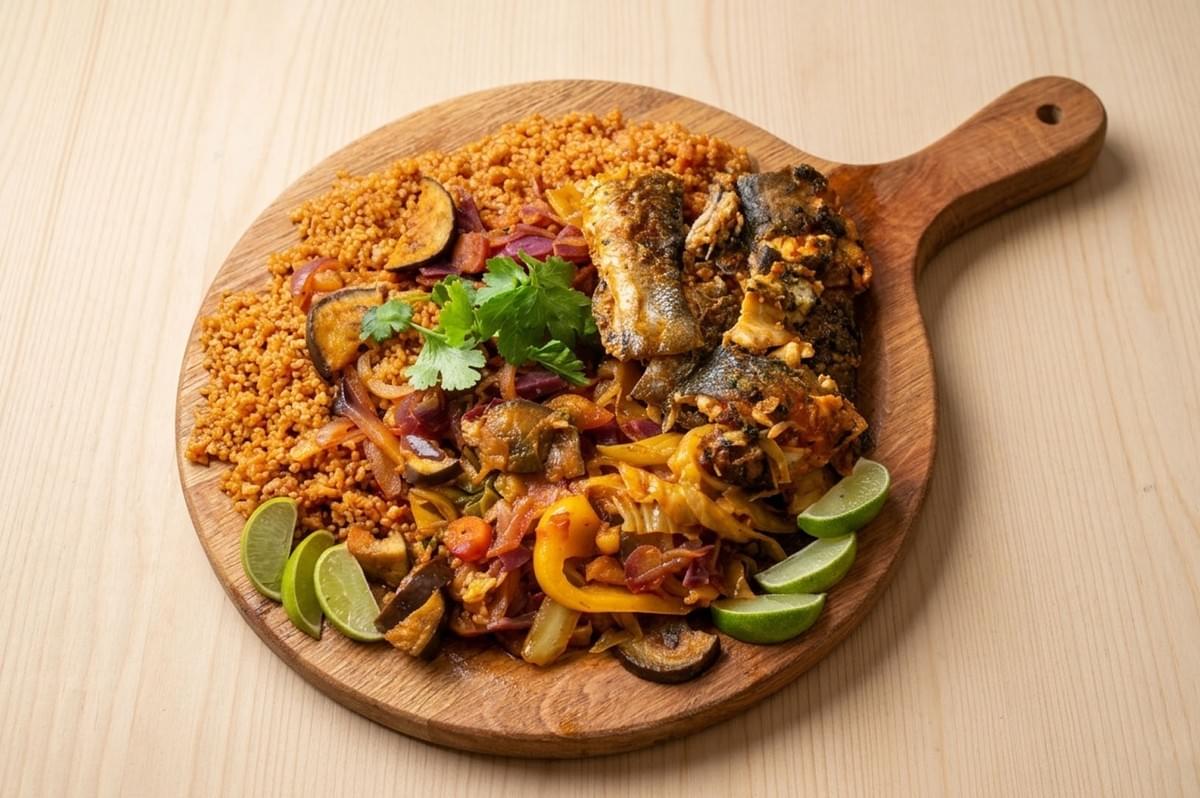 Wooden board with fish, couscous, and stewed vegetables with lime wedges Wooden board with fish, couscous, and stewed vegetables with lime wedges
