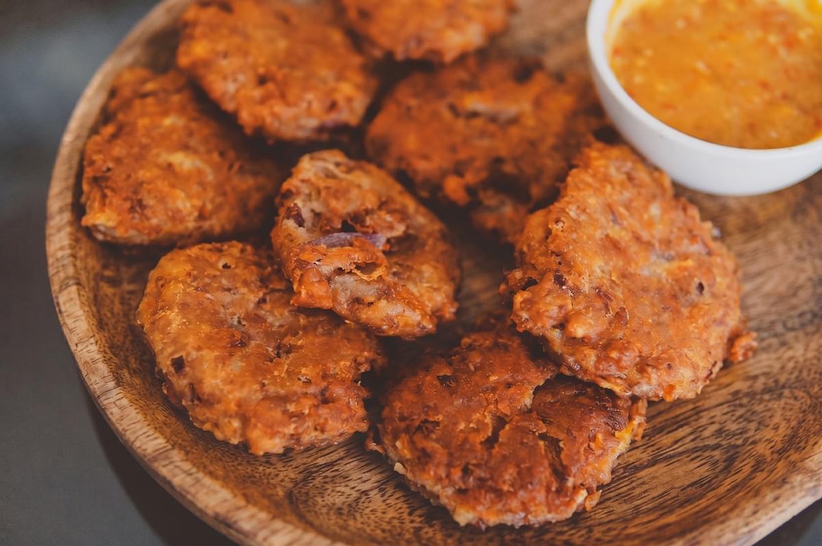 A wooden plate piled with golden-brown fried vegetable fritters served with a side of dipping sauce. A wooden plate piled with golden-brown fried vegetable fritters served with a side of dipping sauce.