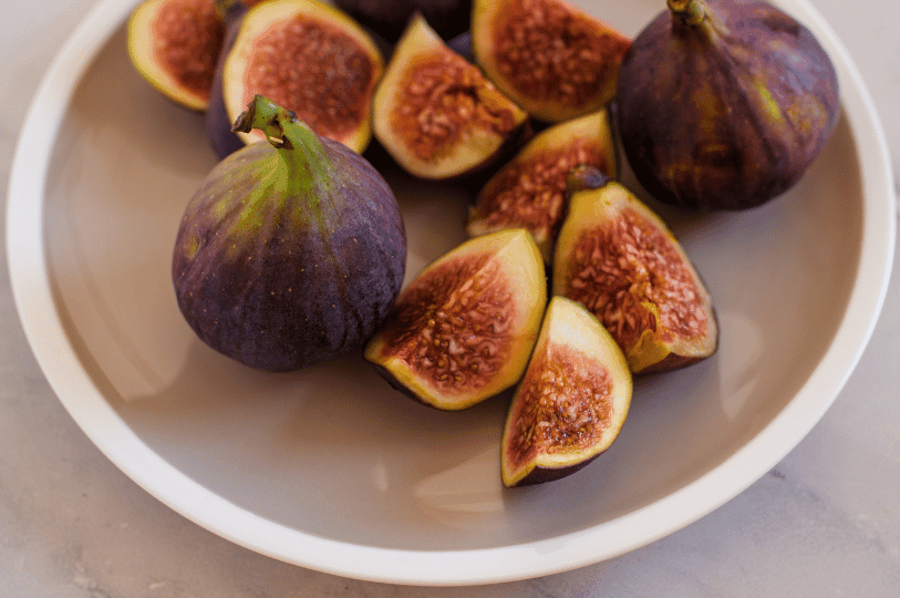 A minimalist overhead view of a white ceramic bowl containing a whole purple fig and several fresh fig wedges, ready for snacking or cooking. A minimalist overhead view of a white ceramic bowl containing a whole purple fig and several fresh fig wedges, ready for snacking or cooking.