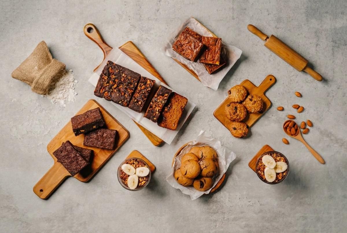 Flat lay display of assorted baked goods including sliced banana bread, brownies, cookies, and parfait cups. Flat lay display of assorted baked goods including sliced banana bread, brownies, cookies, and parfait cups.
