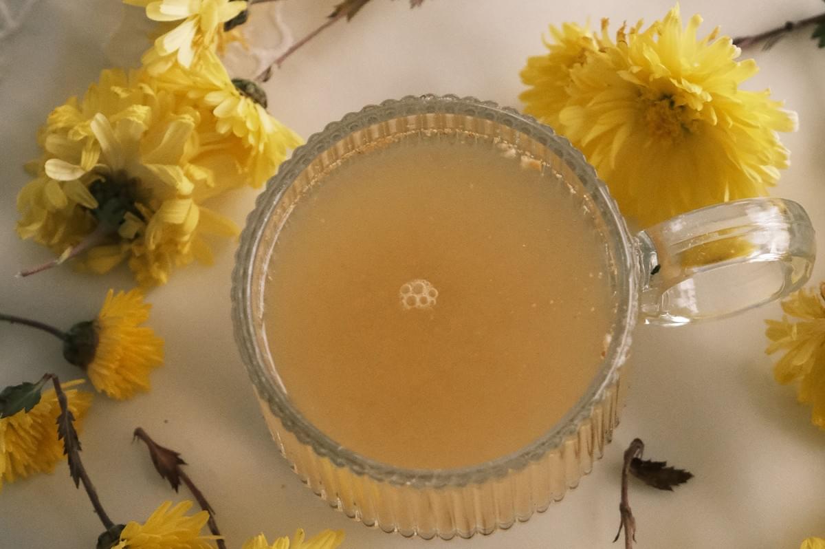 A glass mug of herbal tea surrounded by yellow chrysanthemum flowers. A glass mug of herbal tea surrounded by yellow chrysanthemum flowers.
