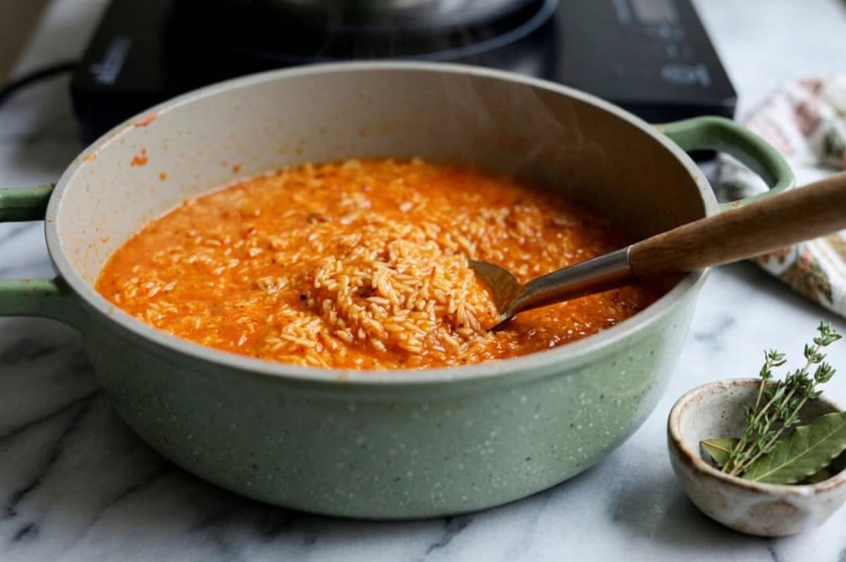 Rice grains simmering in a rich orange tomato stew inside a green cooking pot Rice grains simmering in a rich orange tomato stew inside a green cooking pot