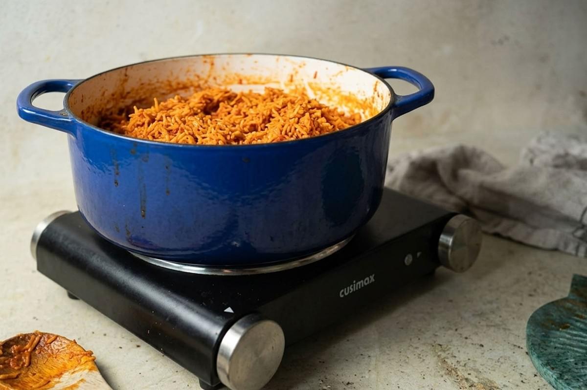 Blue enamel pot filled with cooked orange rice sitting on a black portable burner Blue enamel pot filled with cooked orange rice sitting on a black portable burner