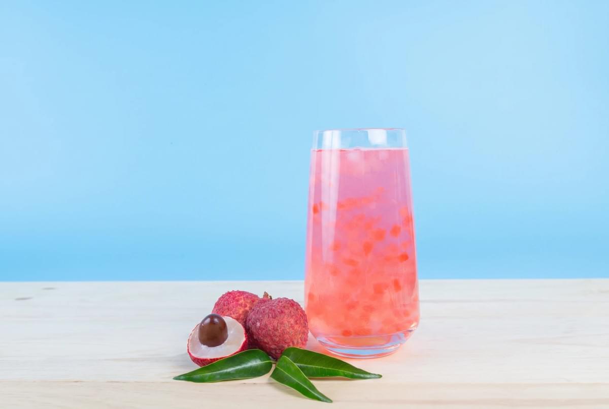 Tall glass of pink lychee drink next to fresh lychee fruits. Tall glass of pink lychee drink next to fresh lychee fruits.