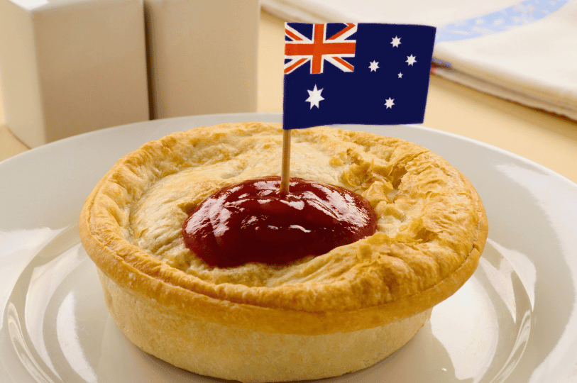 A traditional Australian meat pie served on a white plate, topped with a generous squeeze of tomato sauce (ketchup) and a small Australian flag toothpick. A traditional Australian meat pie served on a white plate, topped with a generous squeeze of tomato sauce (ketchup) and a small Australian flag toothpick.