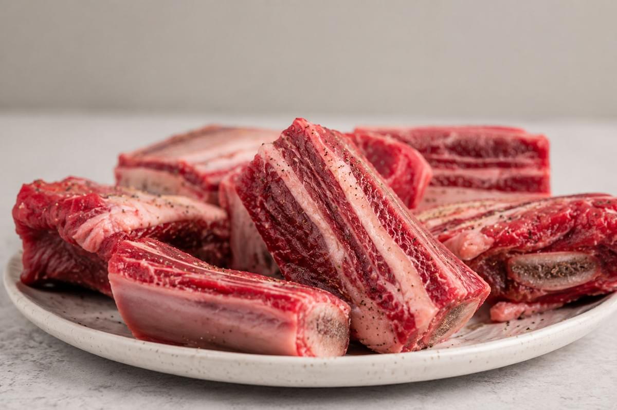 Plate of raw beef short ribs seasoned with salt and pepper, ready for cooking Plate of raw beef short ribs seasoned with salt and pepper, ready for cooking