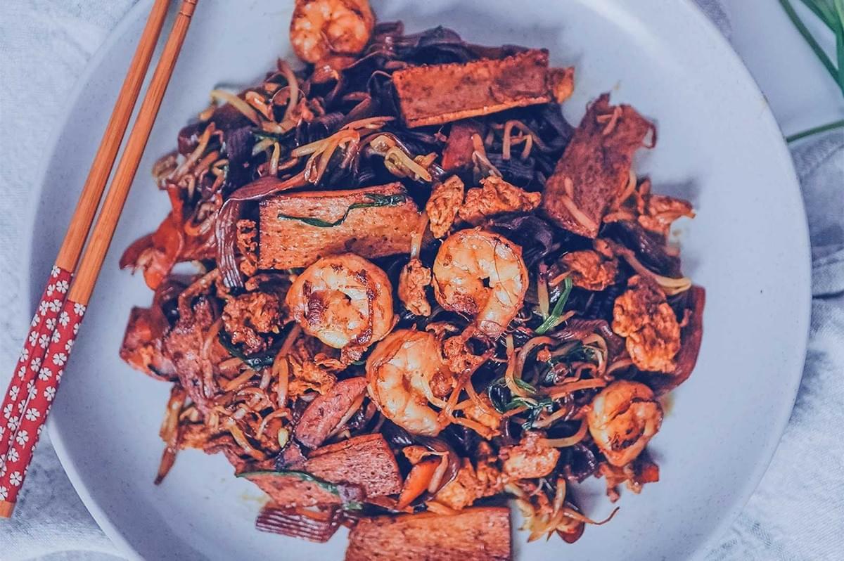 A colorful plate of stir-fried noodles with shrimp, tofu, and vegetables, garnished with herbs. Chopsticks rest beside for an appetizing touch. A colorful plate of stir-fried noodles with shrimp, tofu, and vegetables, garnished with herbs. Chopsticks rest beside for an appetizing touch.