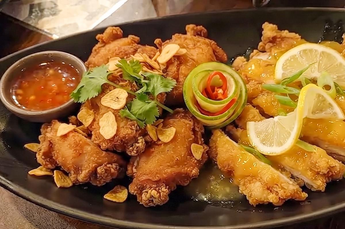 Thai style fried chicken and lemon chicken served together on a black plate. Thai style fried chicken and lemon chicken served together on a black plate.